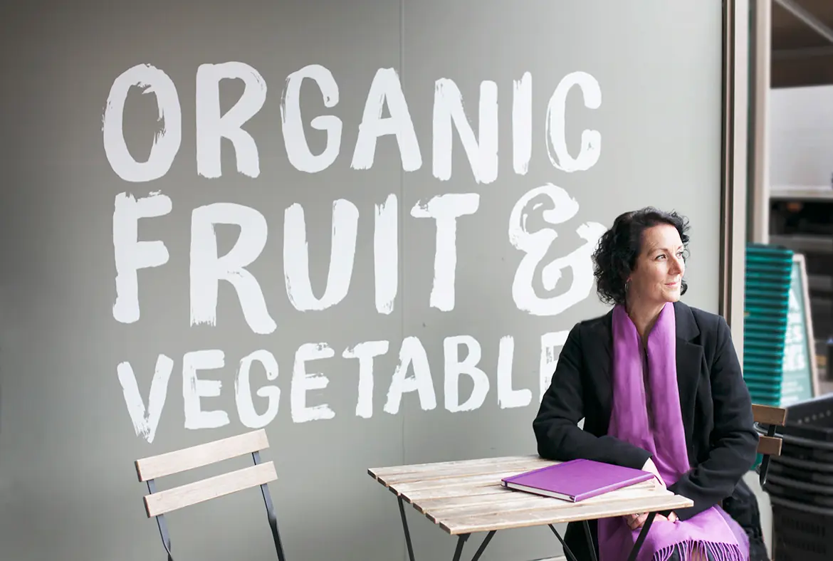 Samantha Flower sitting at a cafe table, with a large sign on the wall reading 